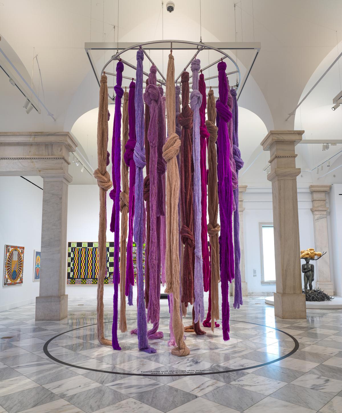 A hanging installation of vibrant locks of fiber in pinks and purples.