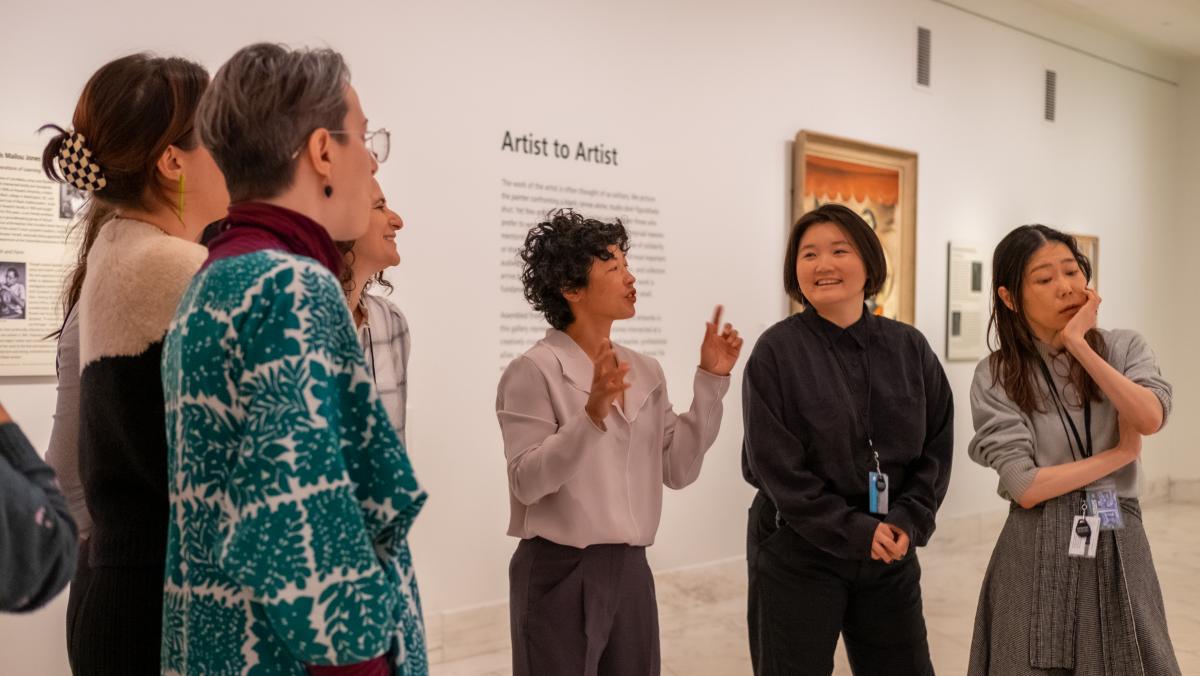Seven people converse in an art gallery