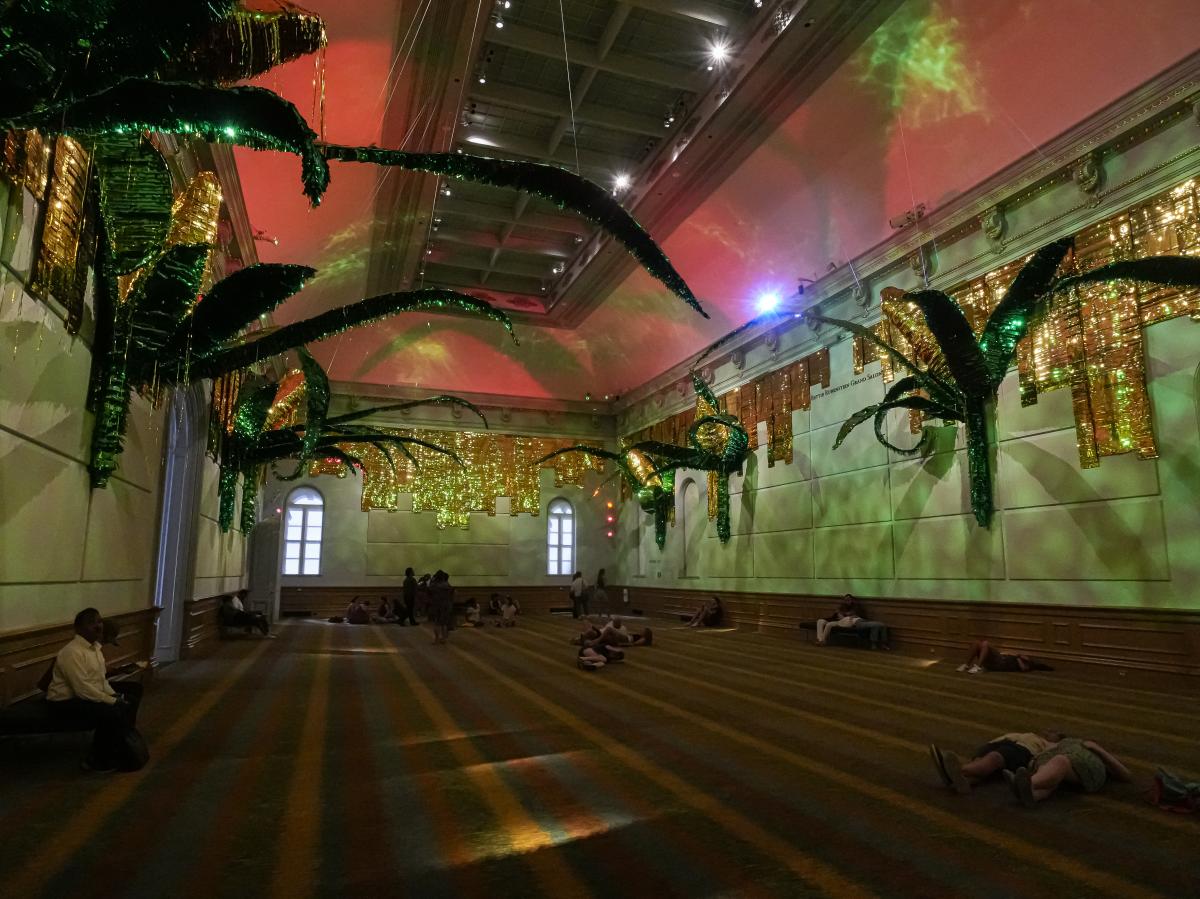 Large-scale installation of corncob piñatas with visitors lying on the carpet.