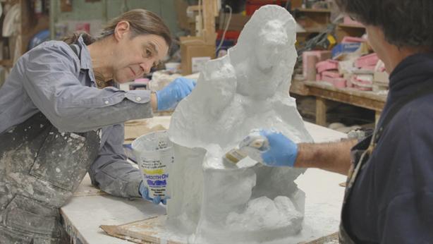Two people work on a plaster cast of sculpture.