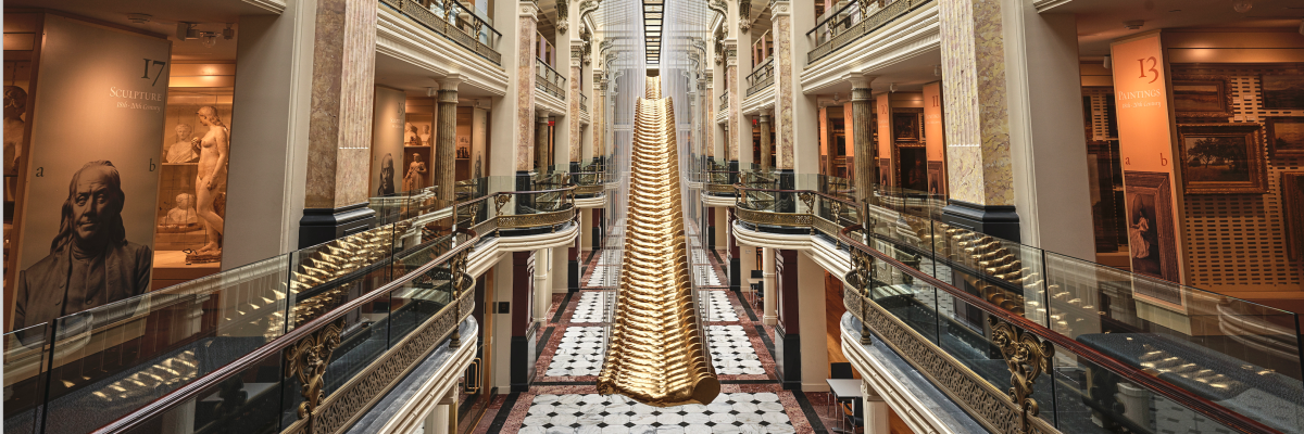 This is a cropped image of the Luce Foundation Center for American Art, a visible art storage space. An artwork featuring gilded arms is centered in the space, with cases of sculptures and paintings on the left and right side.