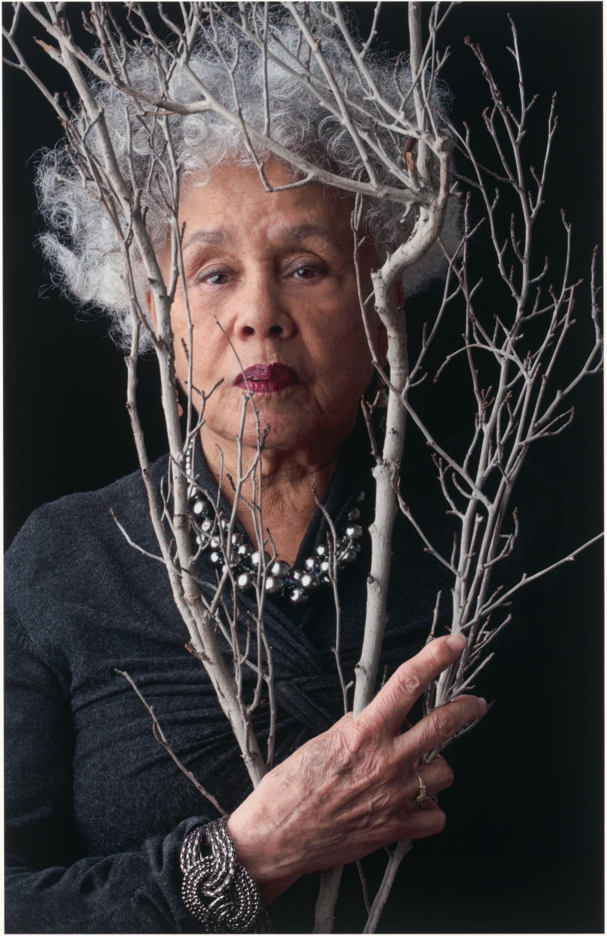 Betye Saar looking through a branch.
