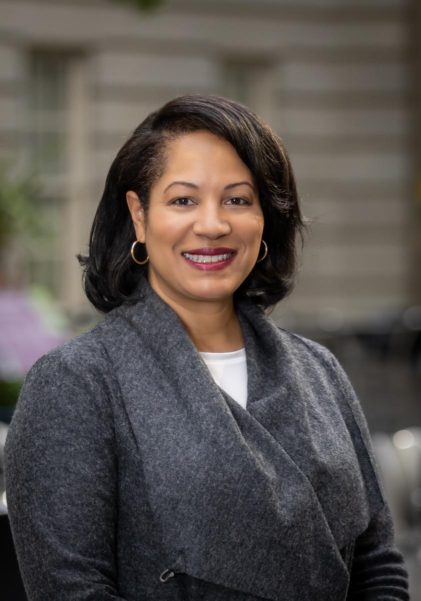 A photograph of an African American woman who is wearing a gray coat. She is smiling.