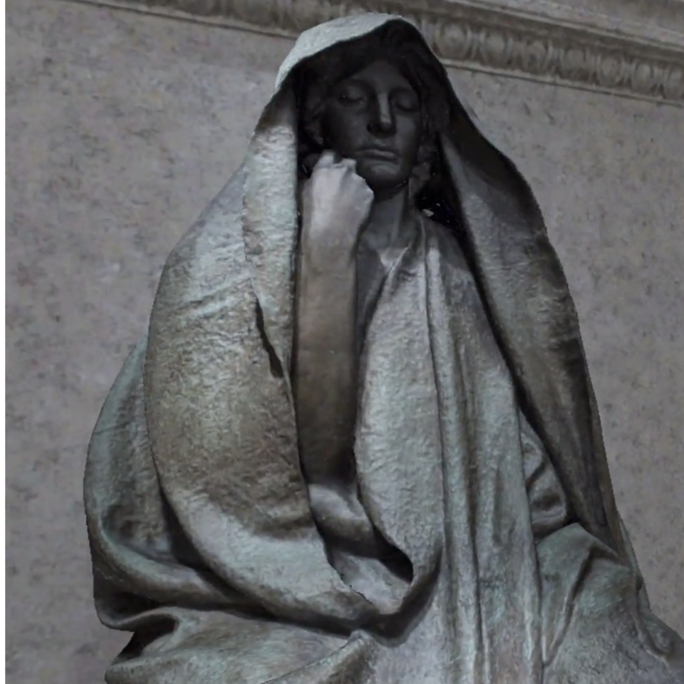 A sculpture of a woman sitting down with her hand on face and a cloth over her head.
