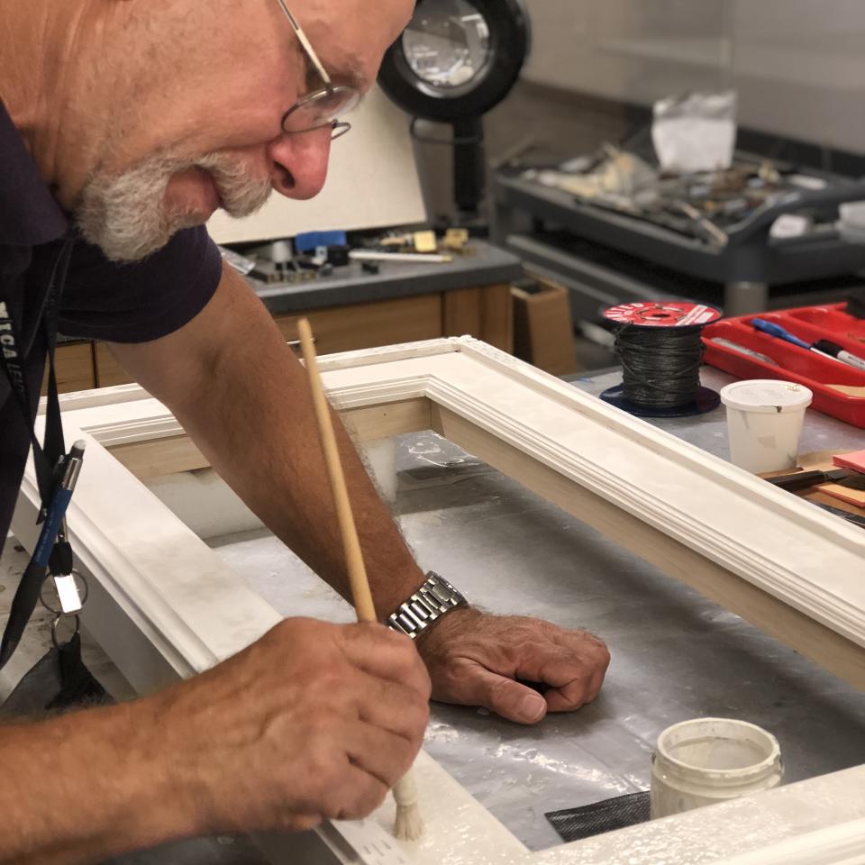 A photograph of a man painting a white frame.
