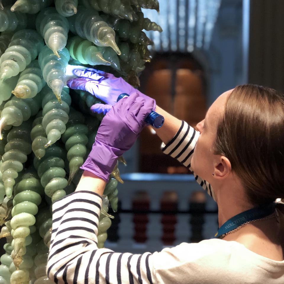 A photograph of a conservator treating a glass sculpture. 