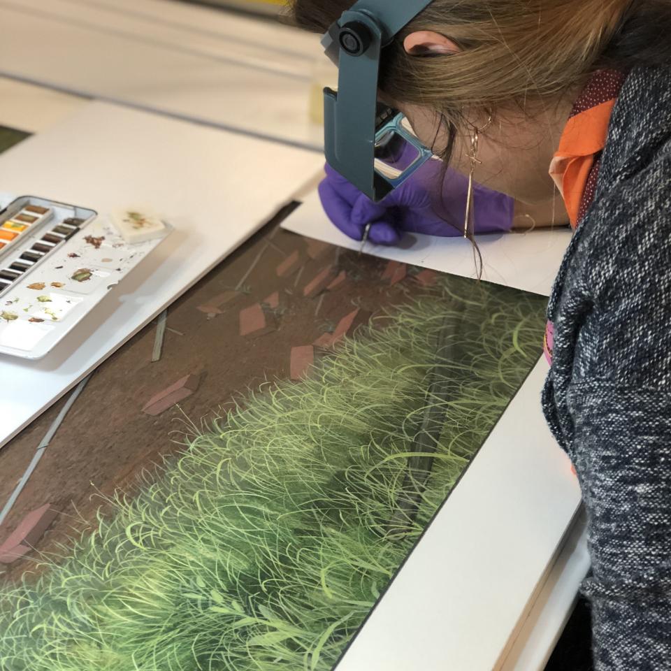 A photograph of a conservator looking over a painting and touching it up. 