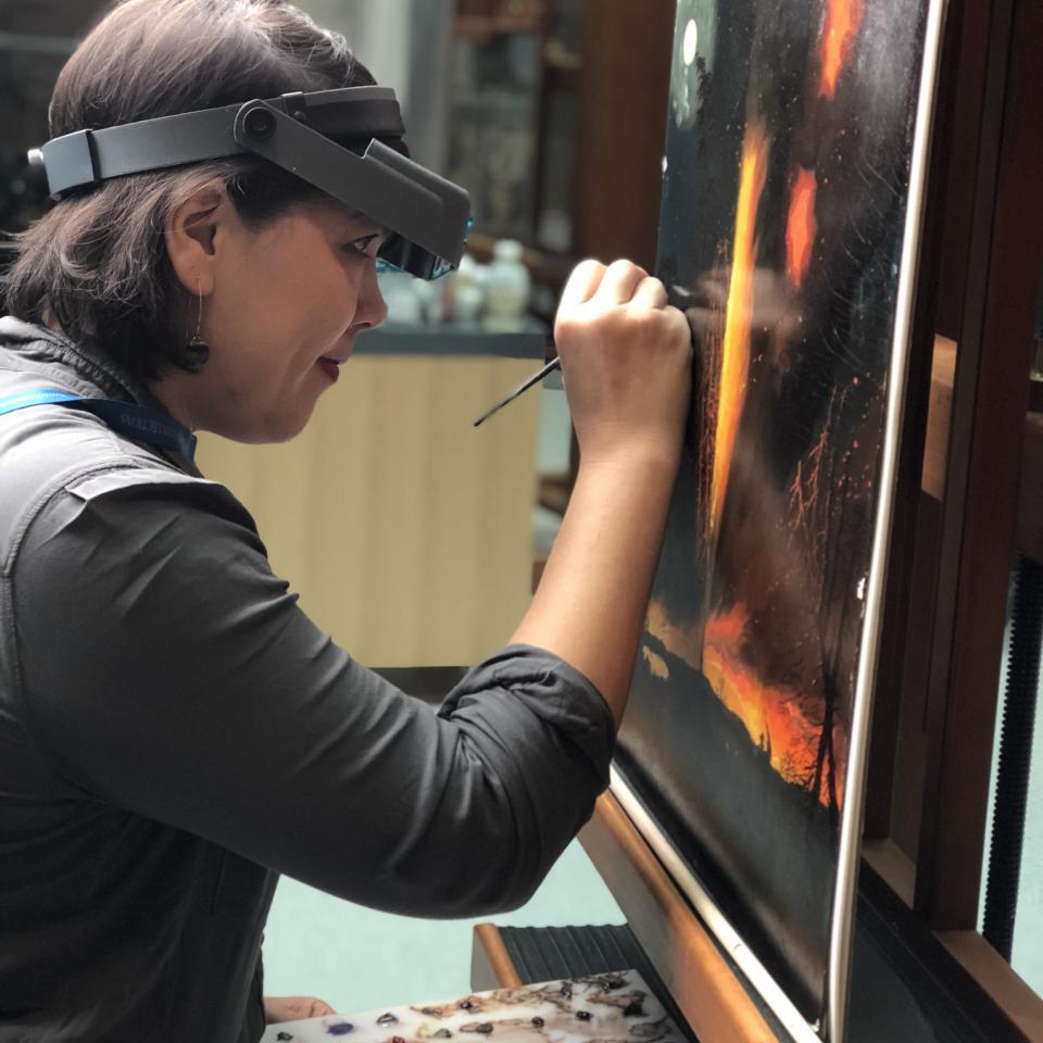 A photograph of a conservator examining and touching up a painting. 