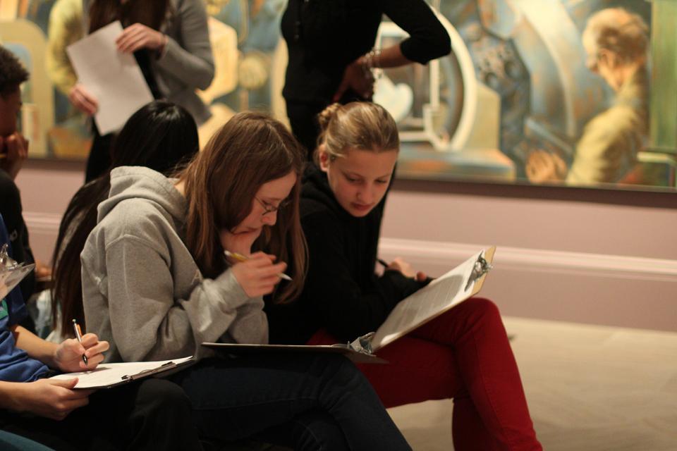 Two teens sitting down and discussing something on a clip board