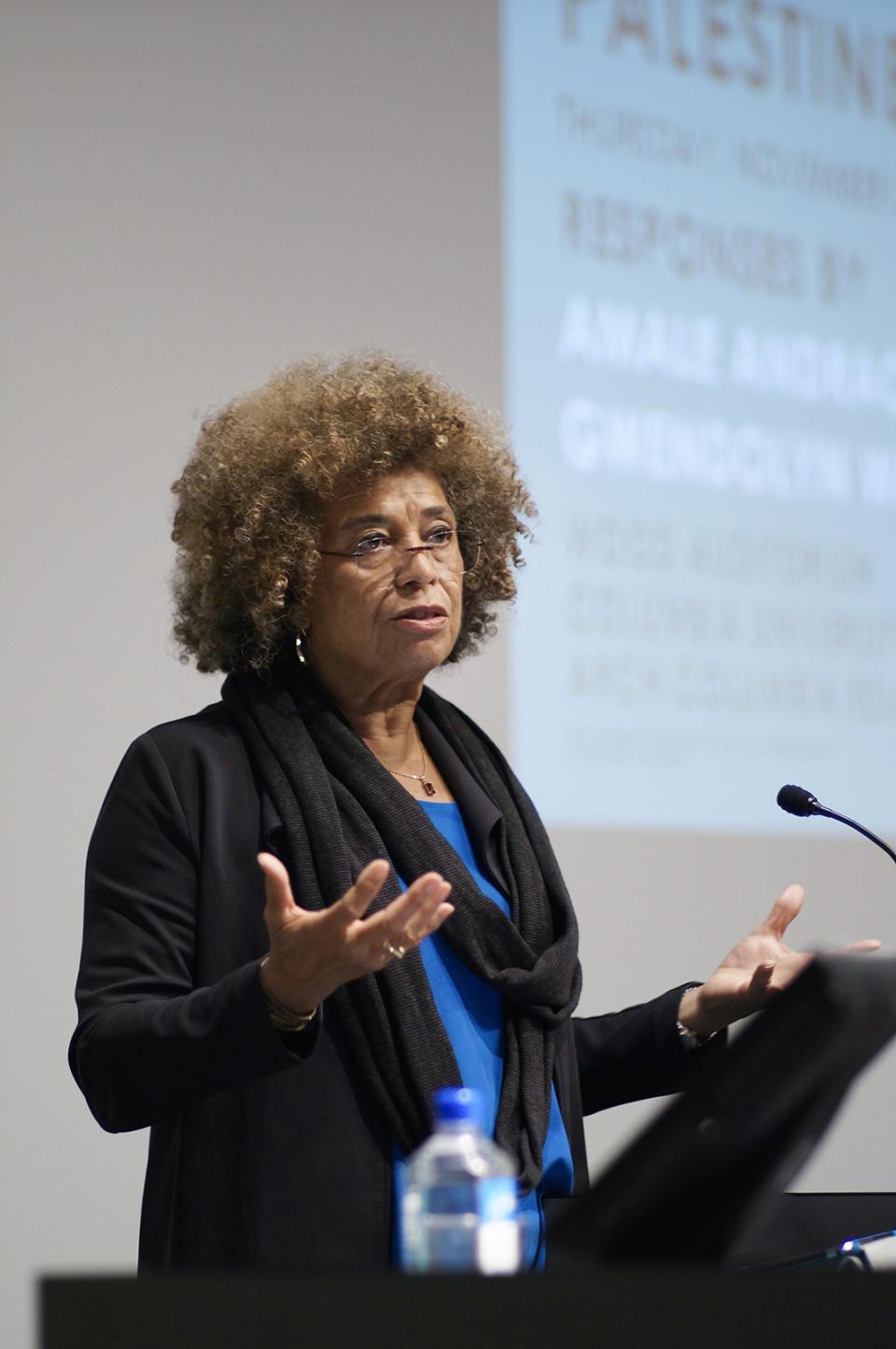 A photograph of a woman standing and lecturing to a crowd