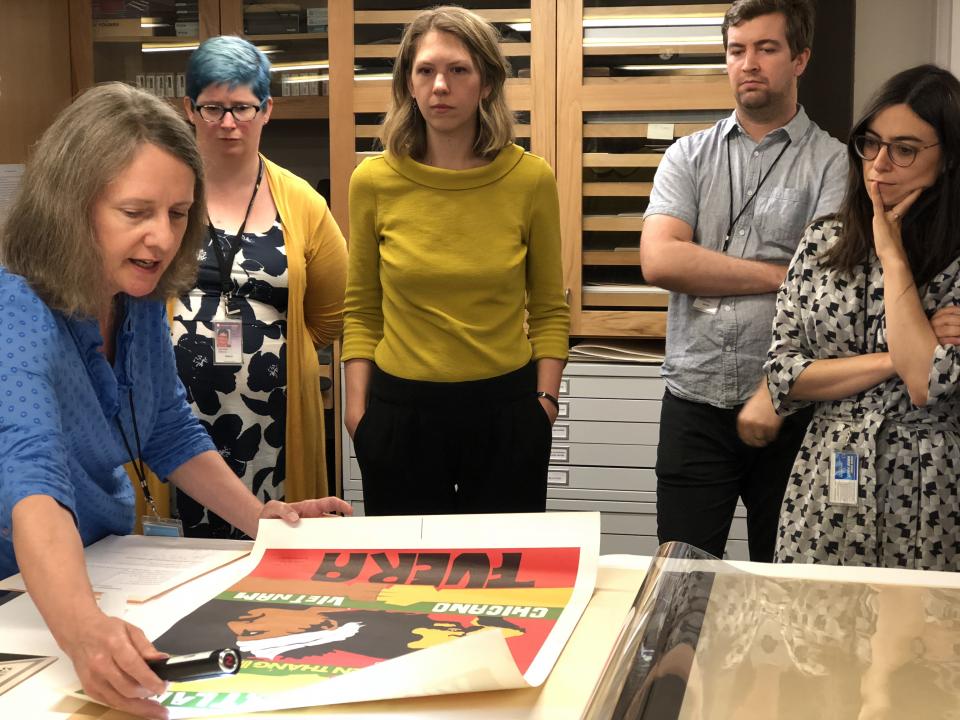 five people looking down at a conservator holding a paper poster