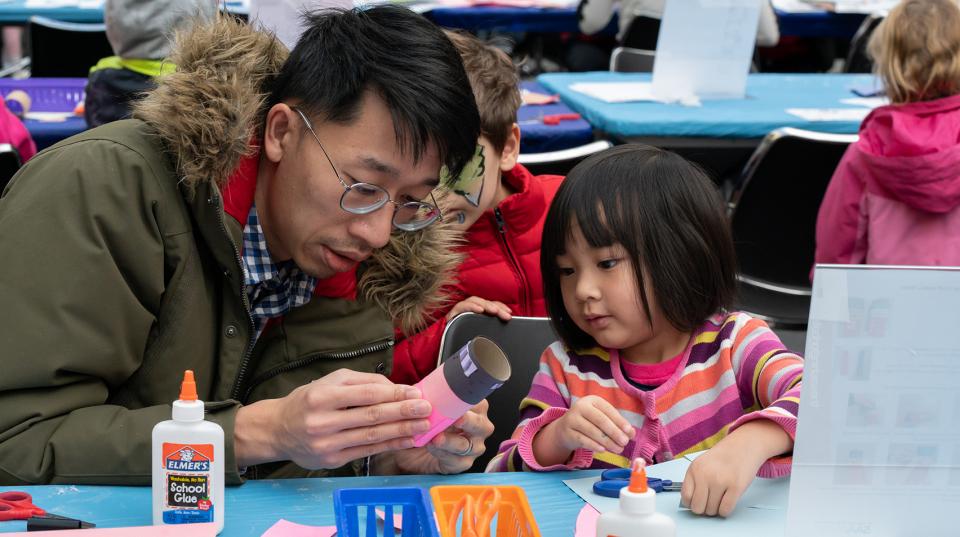 A father and a child sit at a table crafting