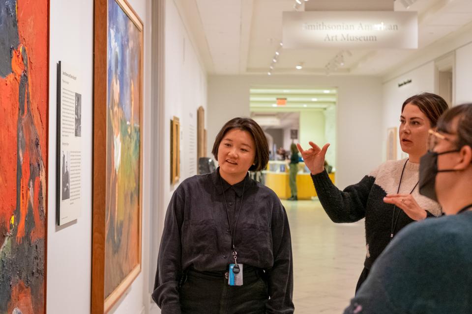 A group of three women looking at and discussing an artwork in the Smithsonian American Art museum.