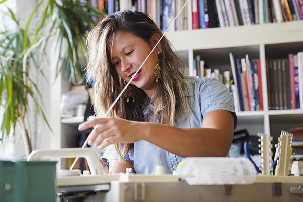 A woman sits making art. White string goes diagonally across her face.