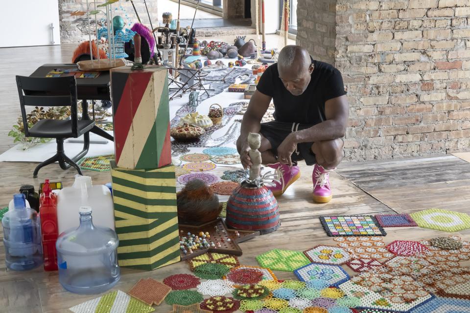 Artist Nick Cave on the floor surrounded by colorful objects.