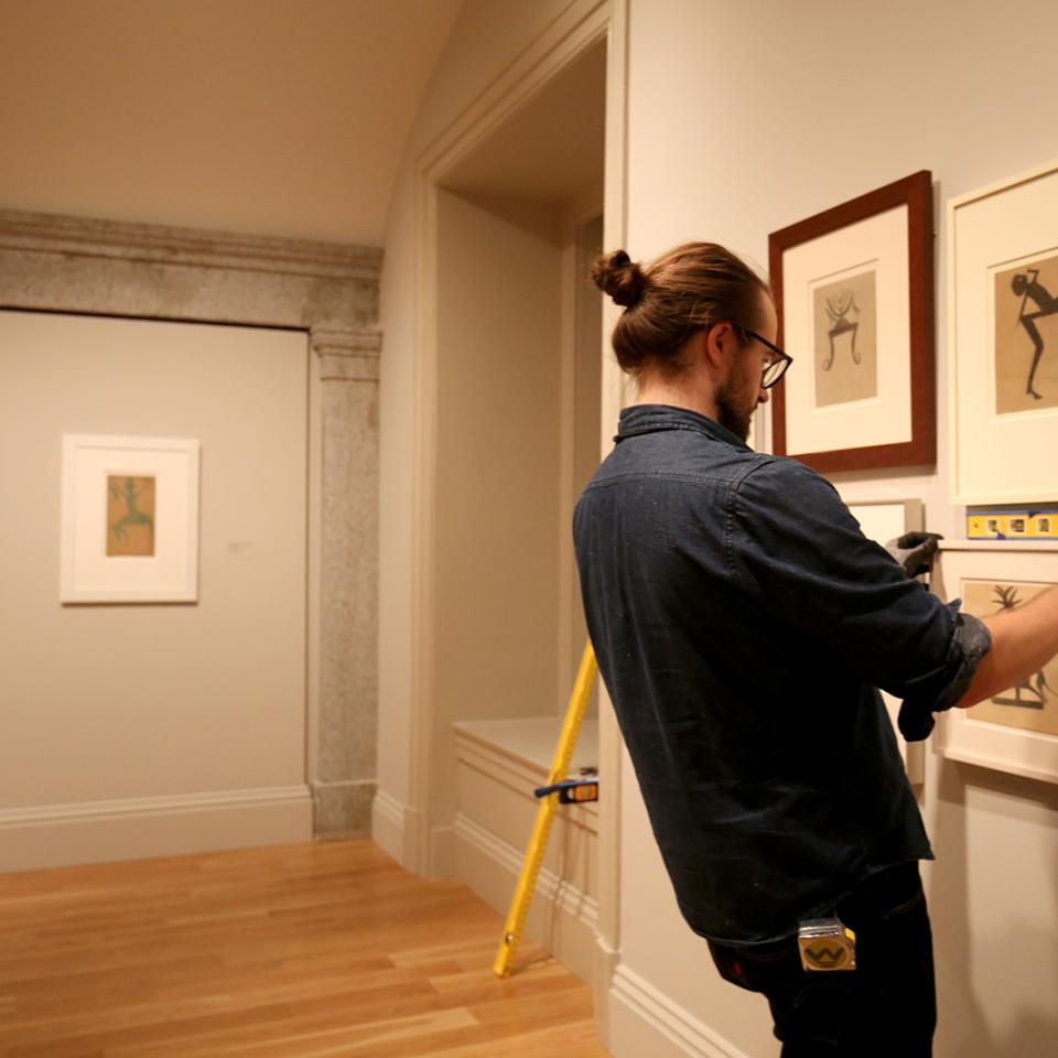 Photo of a man hanging pictures on a gallery wall and checking them with a level.