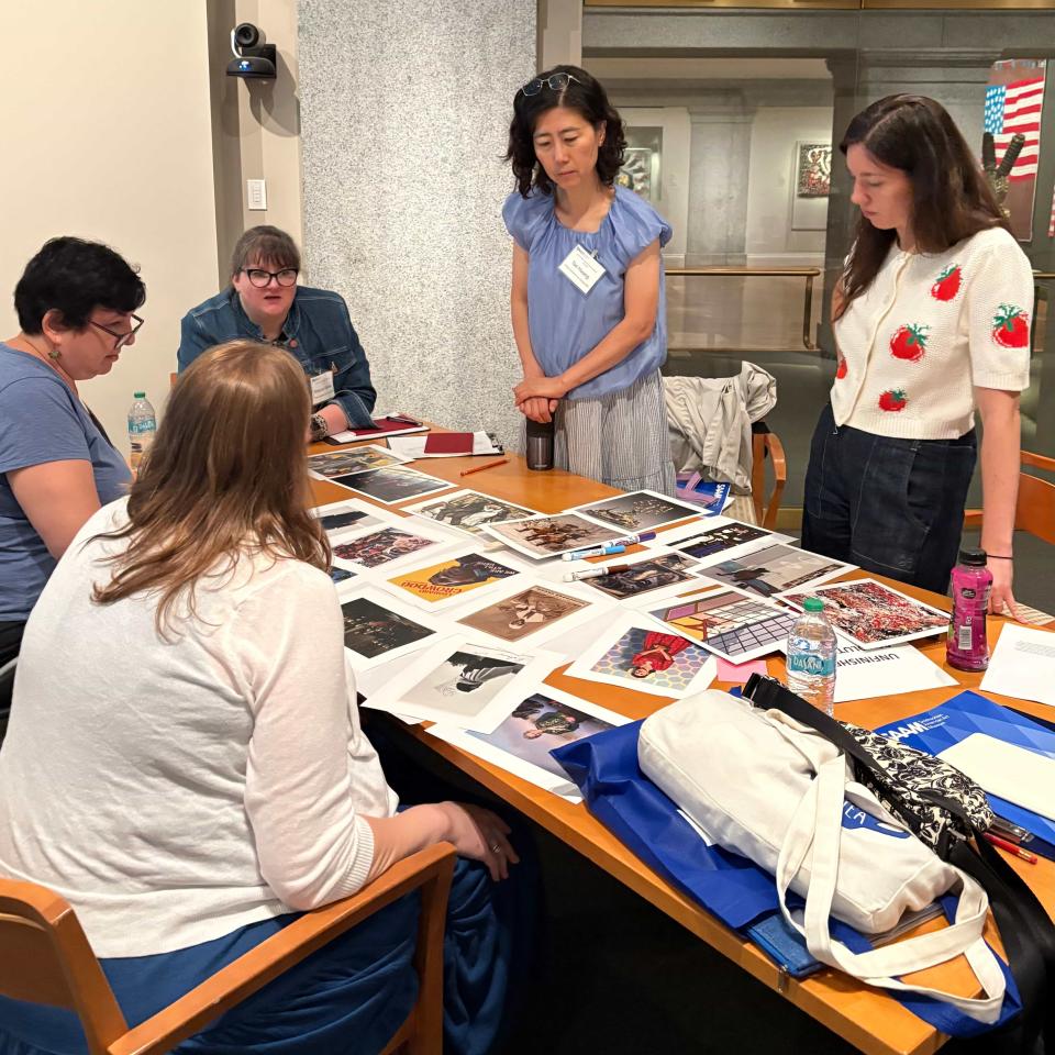 Color photo of people looking at art images arrayed on a confernece room table.