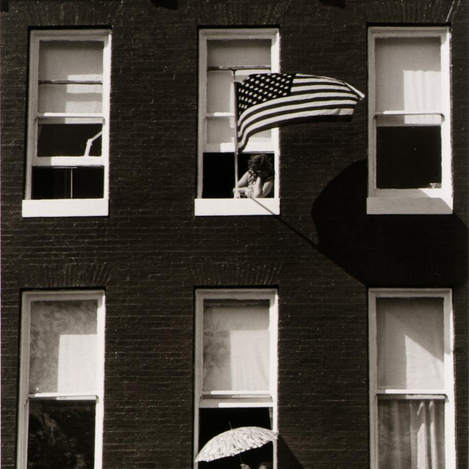 A black and white photograph of two people looking out an apartment facade.