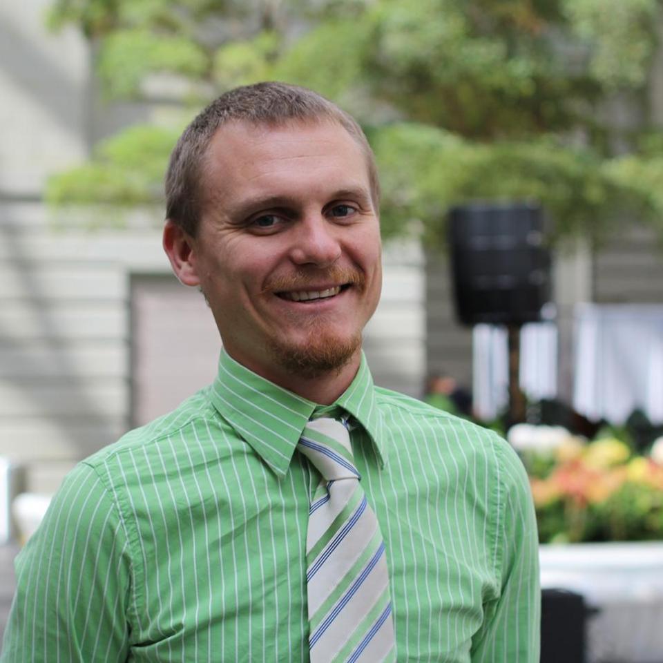 A picture of a man with a green shirt and tie on standing inside a room.