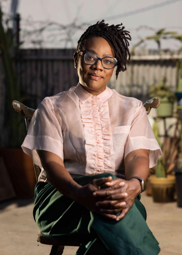 The artist Cauleen Smith sits in a chair in a pink top and green pants
