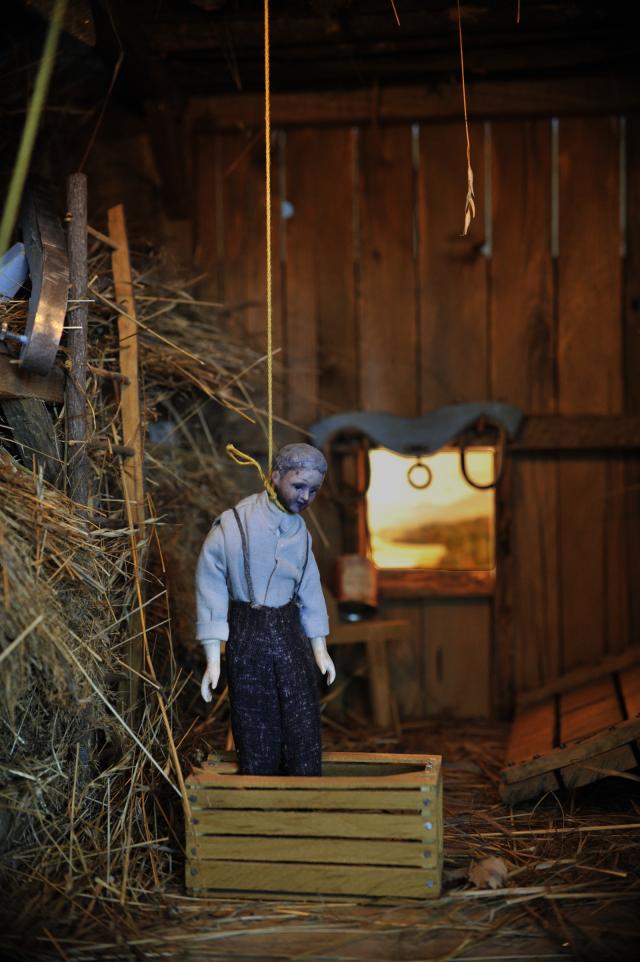 A photograph of a nutshell study of unexplained death showing a detail of a man's death by hanging inside a barn.