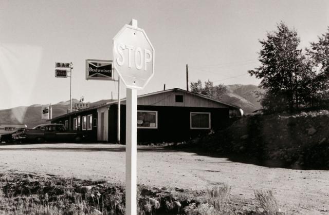 A photograph of a Colorado landscape with stop sign and building taken by automobile.