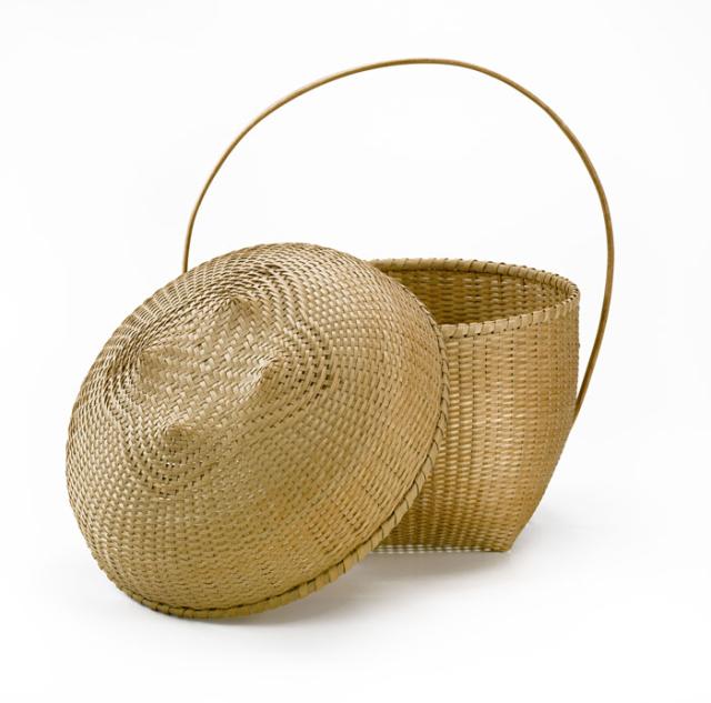 A basket that has a square base that flares our with a circular top and a long thin circular handle. 