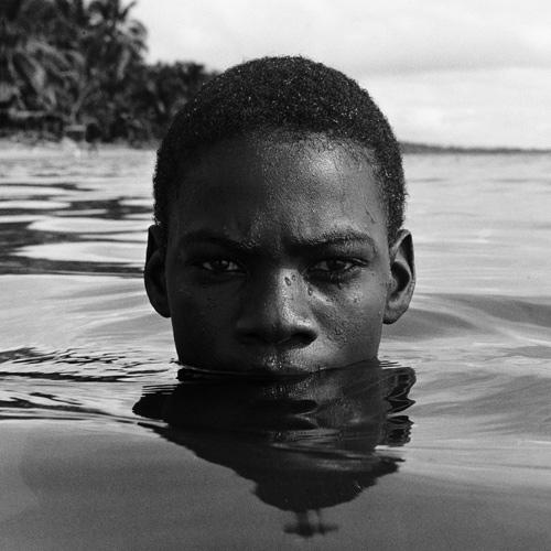 Gleaton's gelatin silver print of a young man swimming in water and only his head is showing with the rest of his body submerged. 