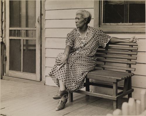 McNeill's gelatin silver print of a woman on a bench outside of a house.