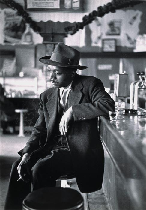 Parks' gelatin silver print of a man sitting at a dinner looking sad and towards the floor.