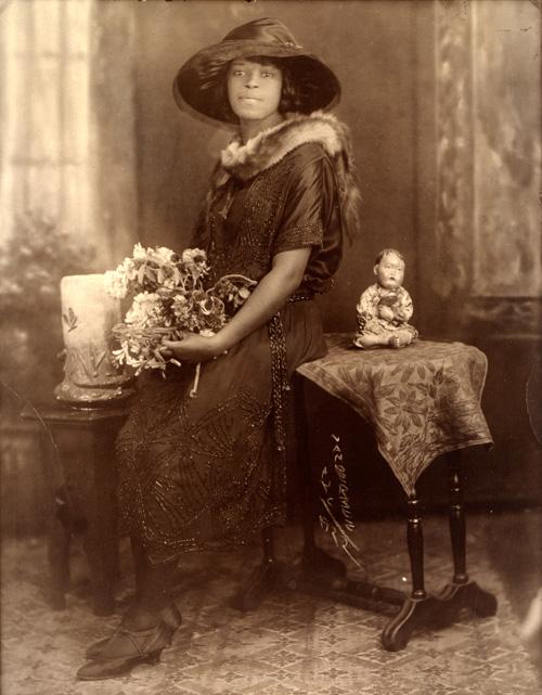 VanDerZee's gelatin silver print of a lady sitting on a table with flowers in her hands.