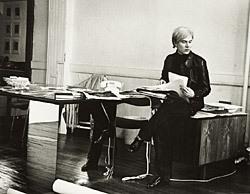 A picture of Andy Warhol sitting at a desk.
