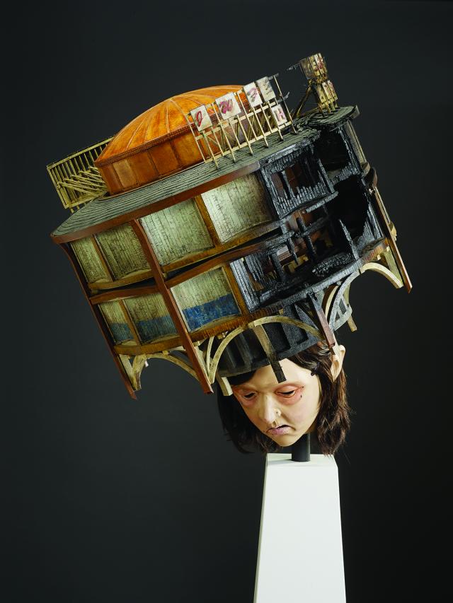 An image of a sculpture with a building on a human head.