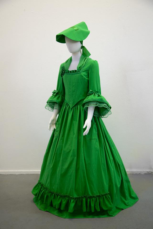An image of a green dress with a colonial hat. 