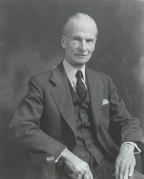 A photograph of a man sitting in a chair in a suit.