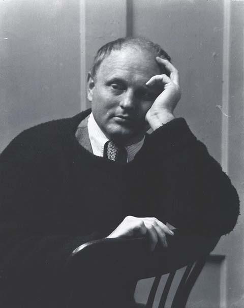 A photograph of a man sitting in a chair with his hand on his face.