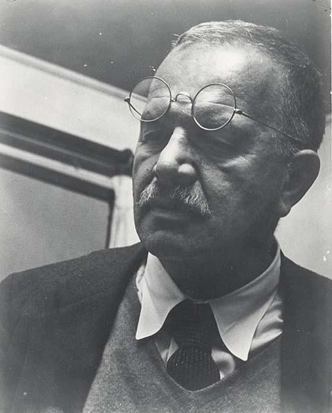 A photograph of a man in a tie with glasses on his forehead.