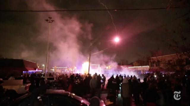 An image taken from an Arthur Jafa film of people gathered around smoke coming from a street.