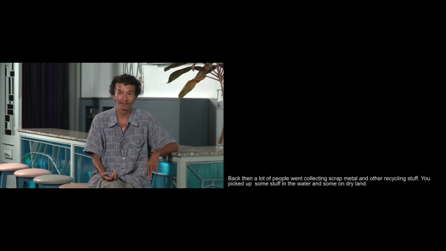 An image of a video with a man sitting down and text next to him on a black screen.