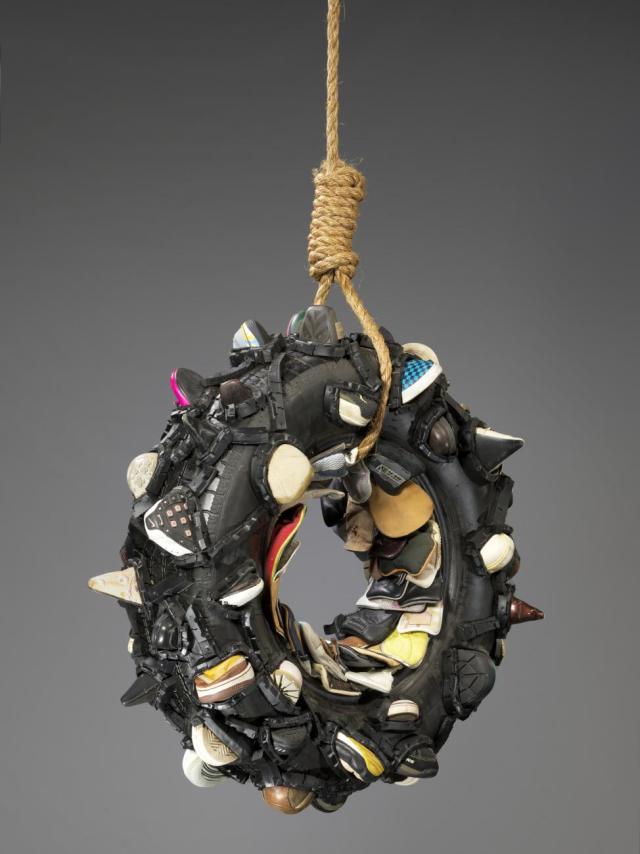 A tire swing with pieces of shoes. 