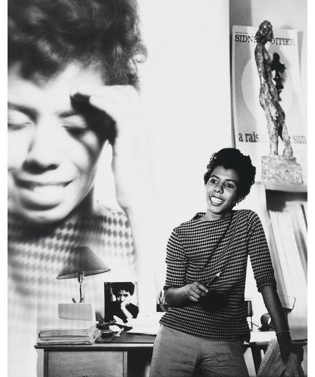 A photograph of a woman standing with an enlarged photograph behind her of herself. 