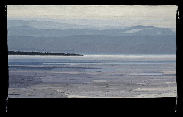 A textile work depicting a landscape with water, land, and mountains.