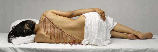 A figure laying on it's side with a diagonal line down it's back with red thread.