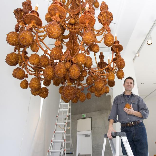A photograph of an artist in a gallery with their work. 