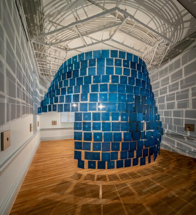 An installation photograph of small cloth indigo hanging from the ceiling. 
