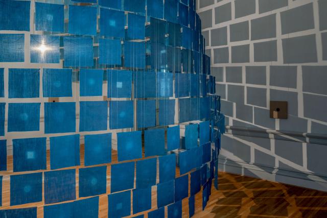 An installation photograph of small cloth indigo hanging from the ceiling. 