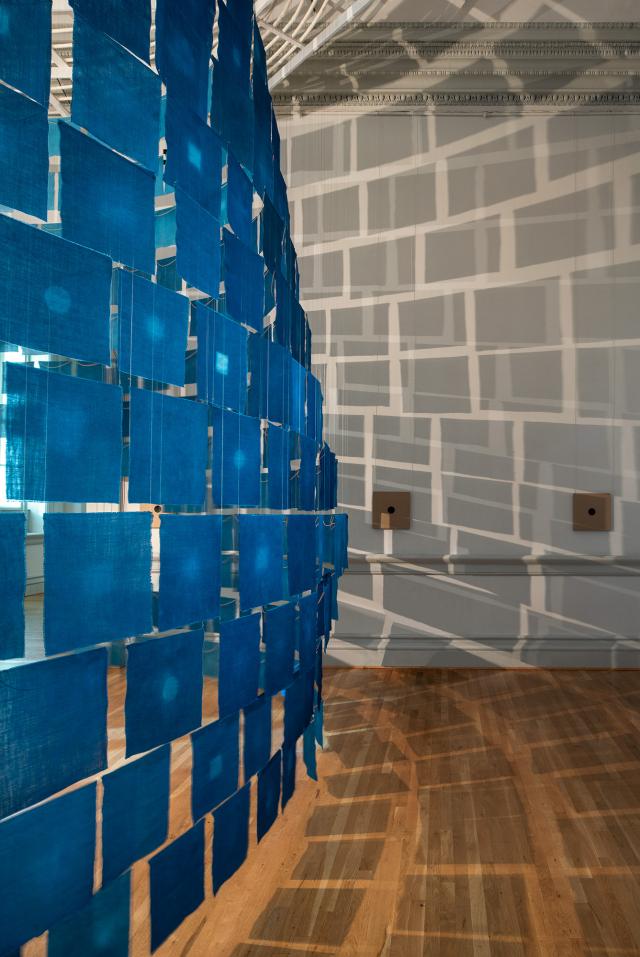 An installation photograph of small cloth indigo hanging from the ceiling. 