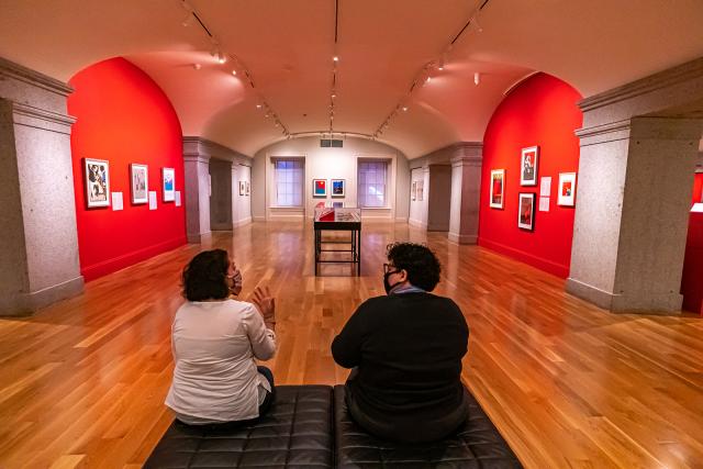 A photograph of an art gallery with two people sitting in the foreground. 