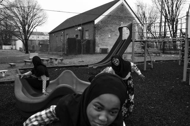 A black and white photos of three African American girls wearing dark hijabs laugh and play on playground equipment.