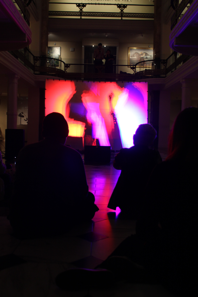 People seated in a dark room look at a colorful illuminated panel.